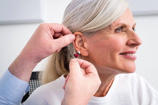 Seniorin bekommt ein modernes Hörgerät eingesetzt, Hörhilfe für besseres Hören im Alter.